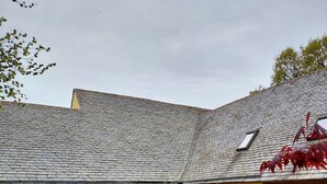 Un bâtiment jaune avec un toit en tuiles, un banc et une cour recouverte de gravier.