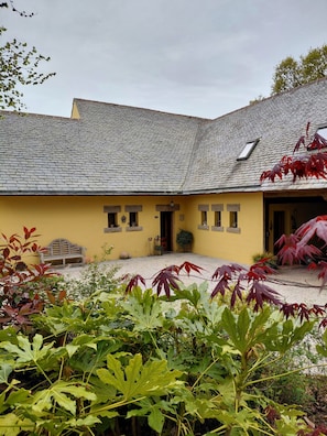 Un edificio giallo con tetto in tegole, una panchina e un cortile in ghiaia.