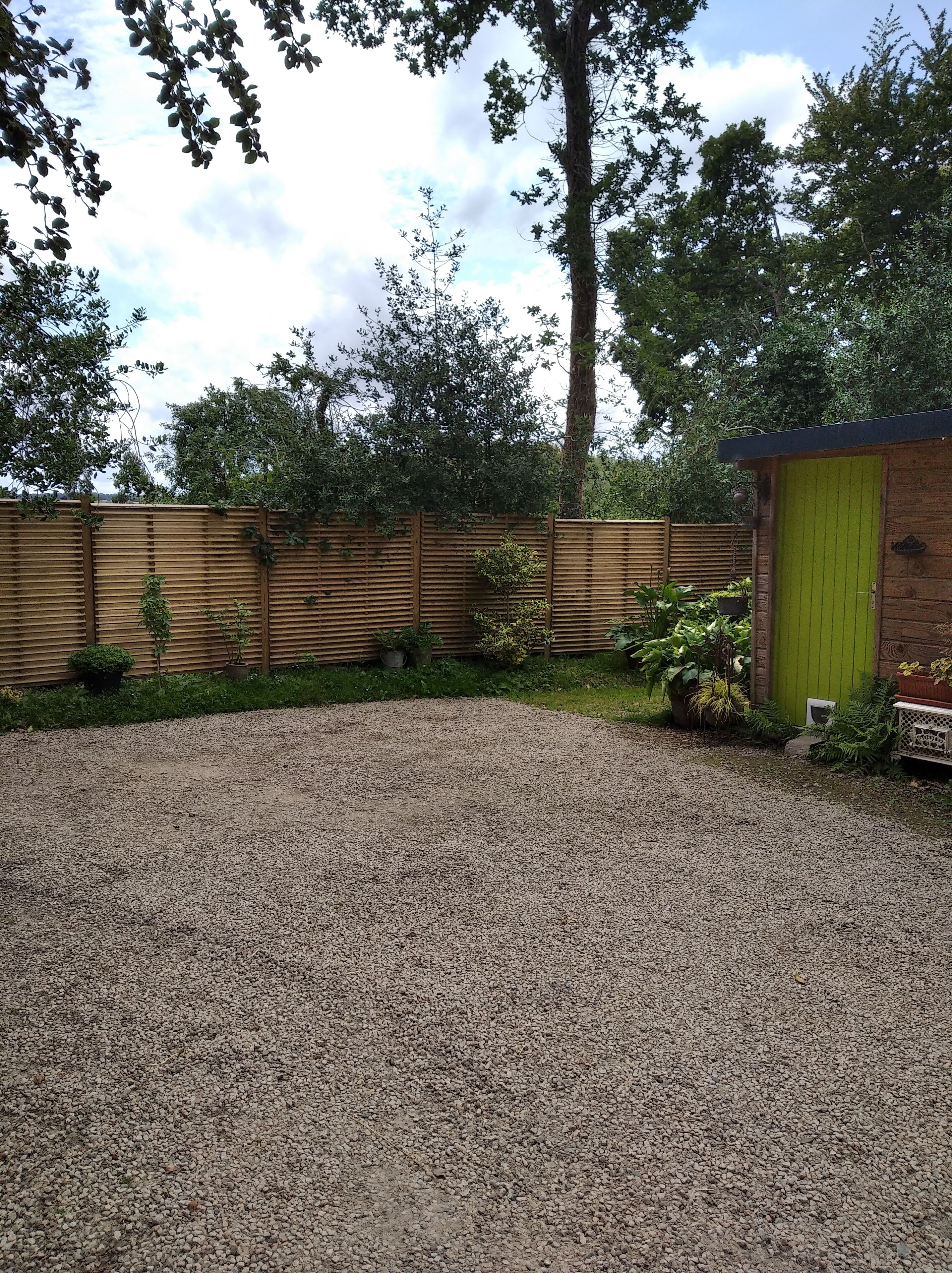 A gravel driveway leading to a wooden fence with potted plants.