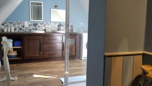 Une pièce avec un plancher en bois, une salle de bain avec une douche, un lavabo et un miroir. Un panneau indiquant le numéro SM 062314 est accroché au mur.