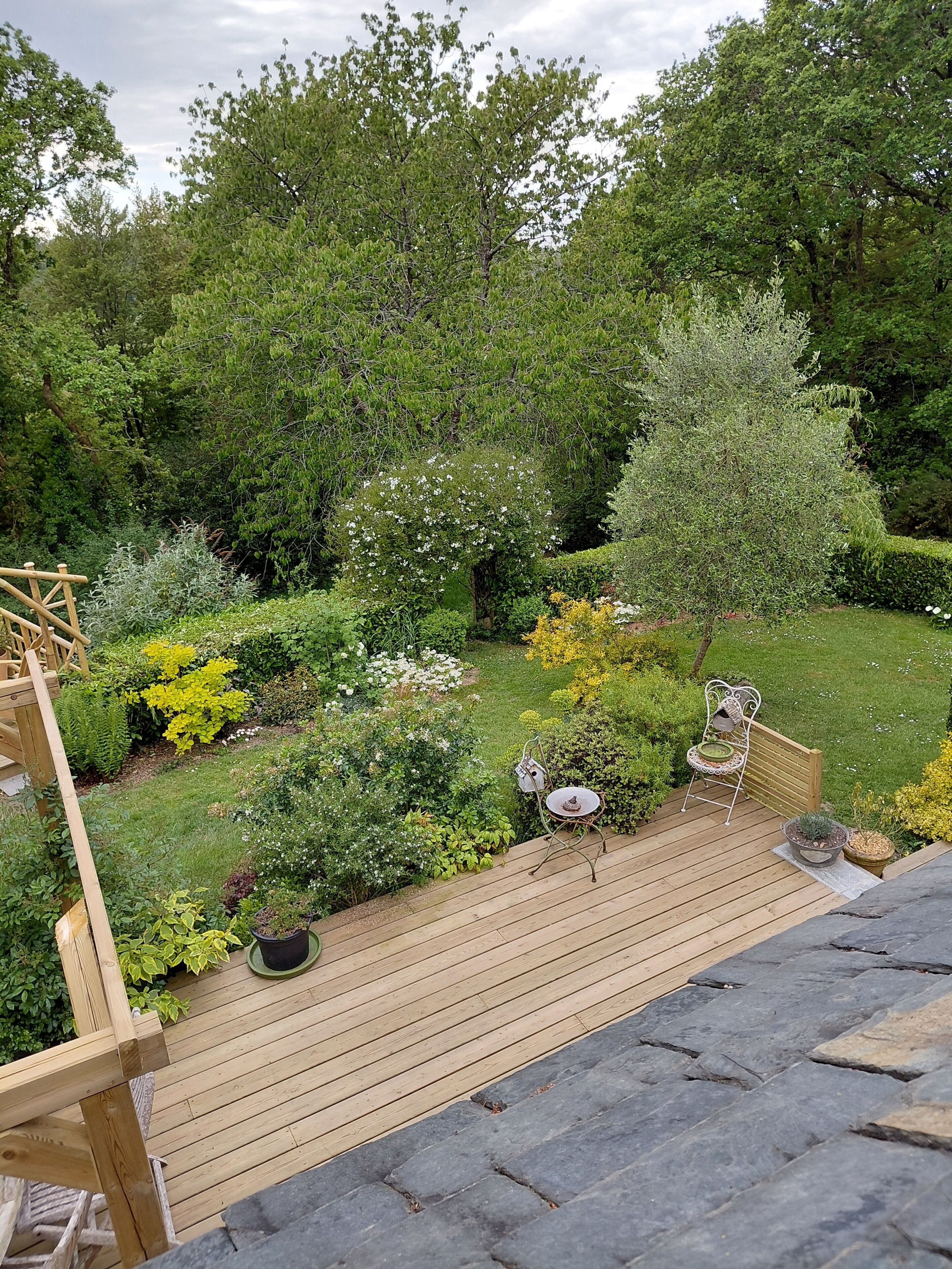 Une terrasse en bois avec un espace salon, entourée d’une végétation luxuriante et d’arbres.