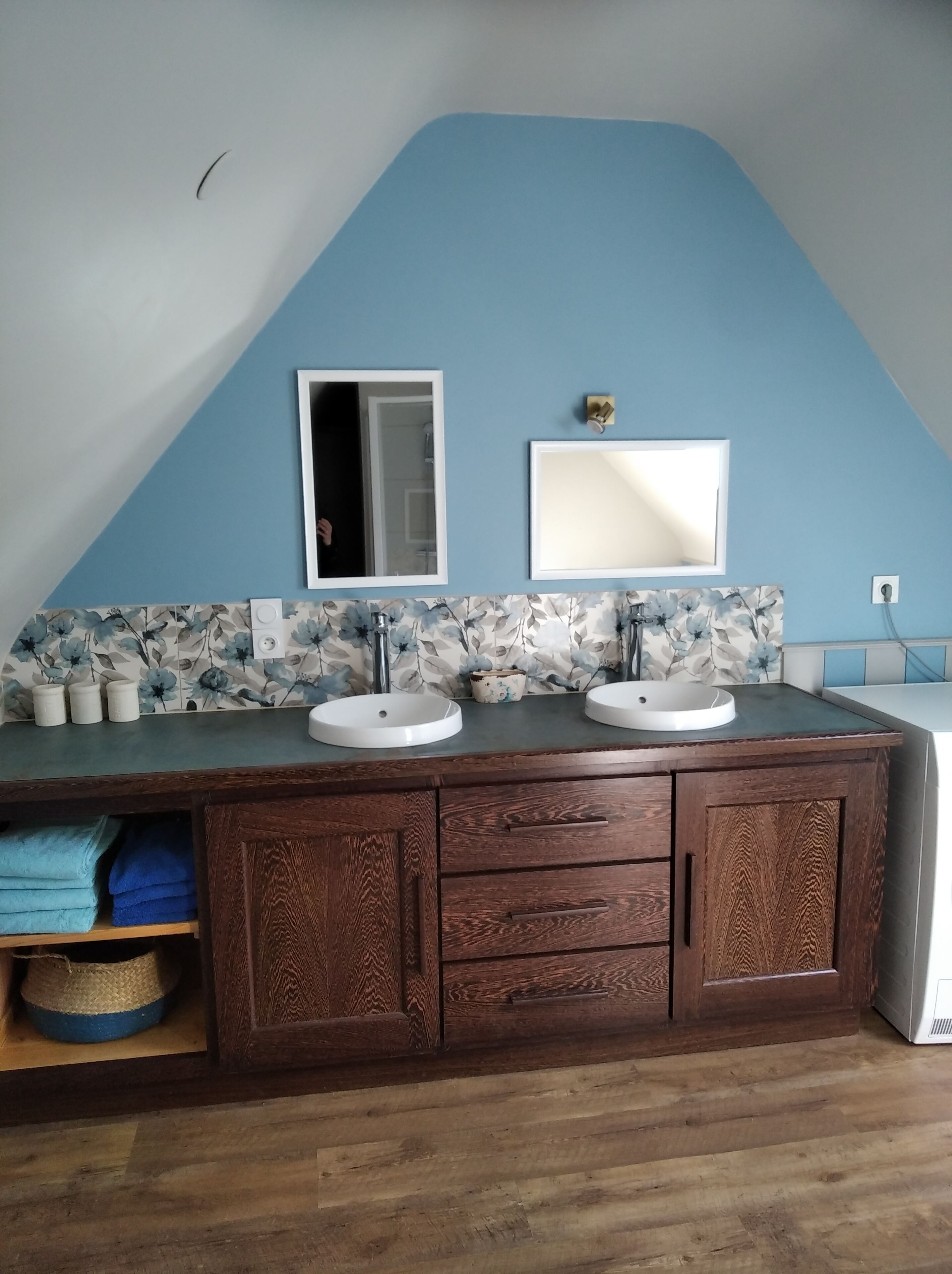 A bathroom with a wooden vanity, two sinks, a mirror, and a floral backsplash.