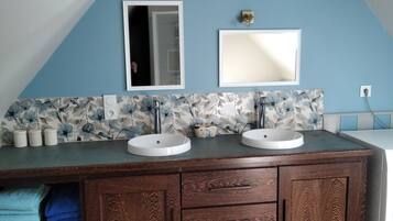 A bathroom with a wooden vanity, two sinks, a mirror, and a floral backsplash.