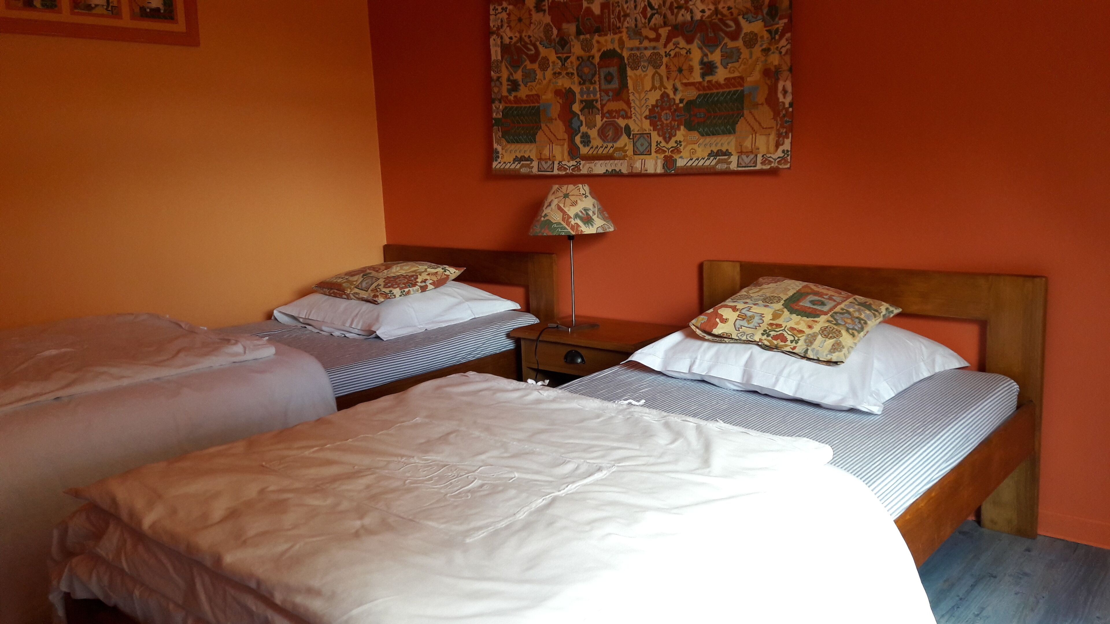 Una habitación con dos camas individuales, una mesita de noche con lámpara y un tapiz decorativo en la pared.