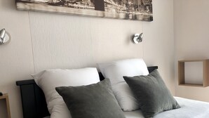 A bed with white and gray pillows, a wooden headboard, and a wall-mounted light fixture. - APARTMENT T2 DOWNTOWN IDEAL CURES SKI RIDE FREE WIFI (Mont-Dore)
