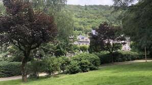 A lush green park with mature trees and a well-maintained lawn. In the background, there is a large house with a classic architectural style, surrounded by dense foliage. - APARTMENT T2 DOWNTOWN IDEAL CURES SKI RIDE FREE WIFI (Mont-Dore)