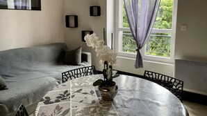 A room with a gray sofa, a round table with a floral tablecloth, and a window with purple curtains. - APARTMENT T2 DOWNTOWN IDEAL CURES SKI RIDE FREE WIFI (Mont-Dore)