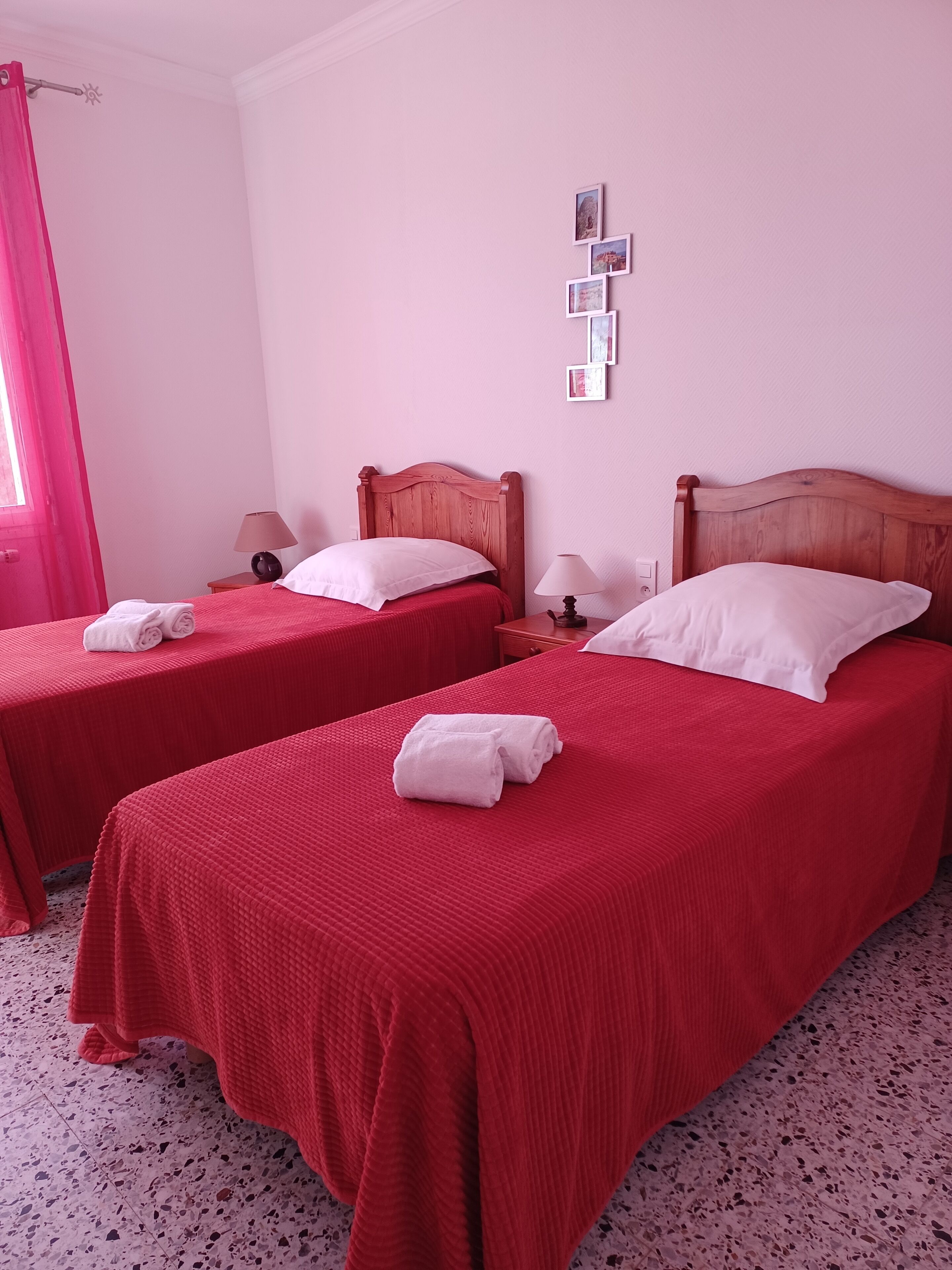 A hotel room with two beds, each with a red bedspread and white pillows, a wooden headboard, a nightstand with a lamp, and a wall-mounted picture frame.