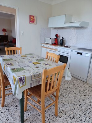 A compact kitchen with white appliances, a dining table with a floral tablecloth, and a patterned floor.