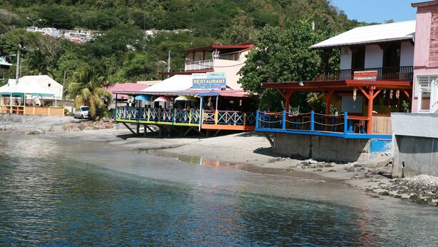 A waterfront restaurant with outdoor seating and a view of the water. - House (Deshaies)