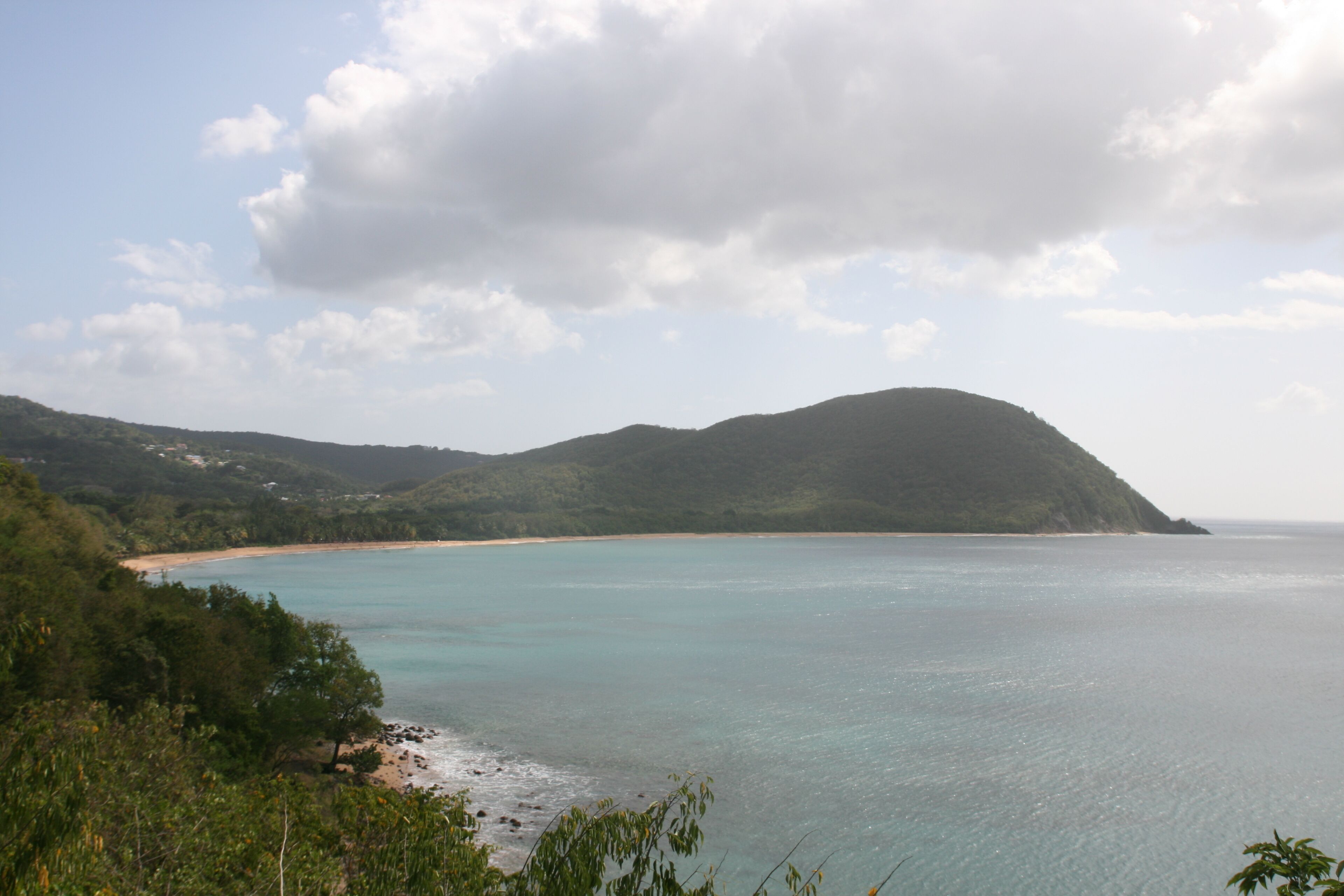 Paisaje costero con una playa, cielo despejado y una montaña.