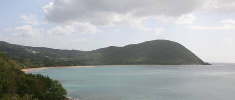 Paisaje costero con una playa, cielo despejado y una montaña.
