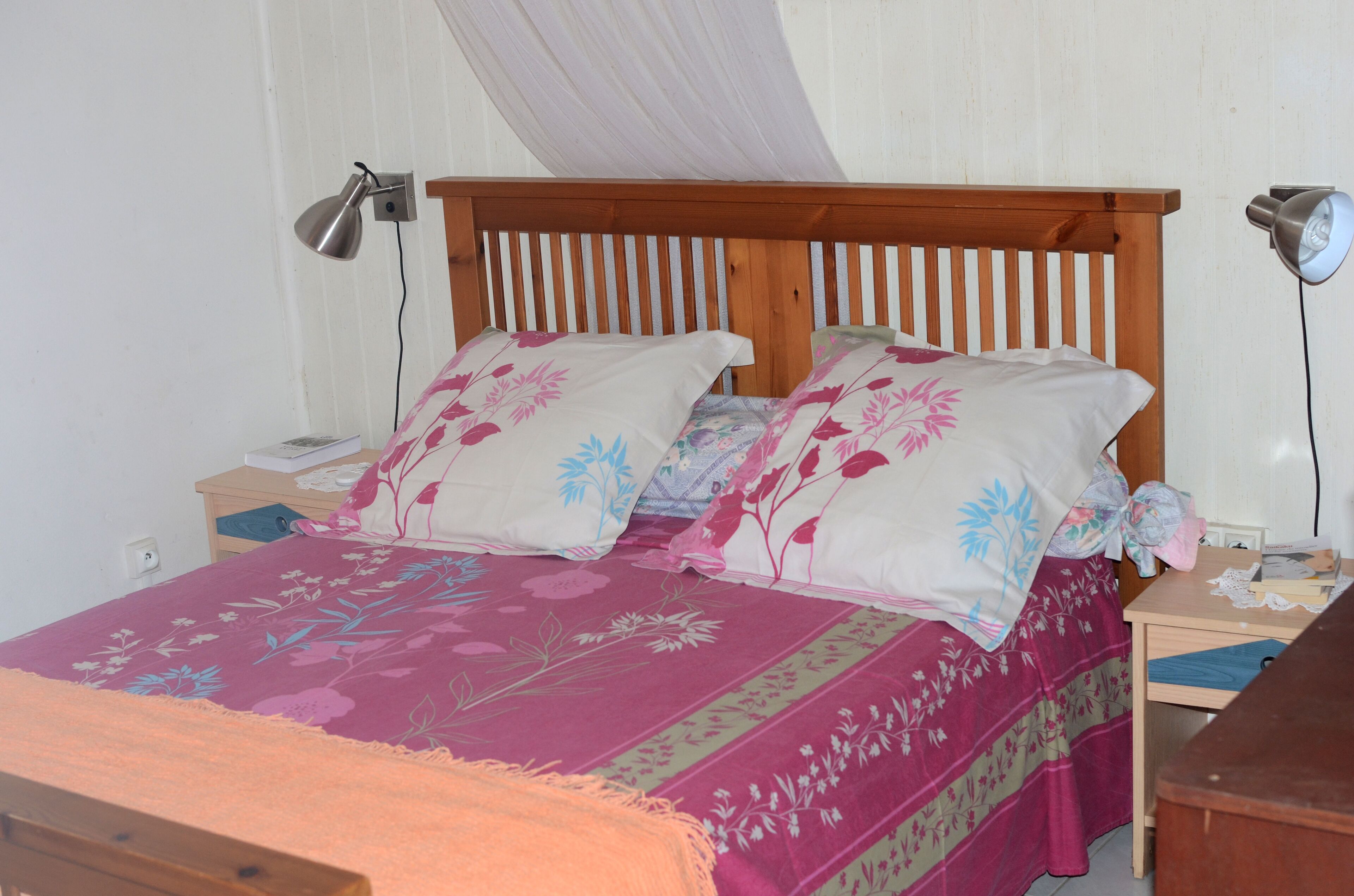 A bed with a wooden headboard, two bedside lamps, a nightstand with a lamp, and a bedside table with a lamp.