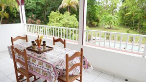 A dining area with a table set for four, surrounded by wooden chairs, overlooking a lush garden and a pool. - House (Deshaies)