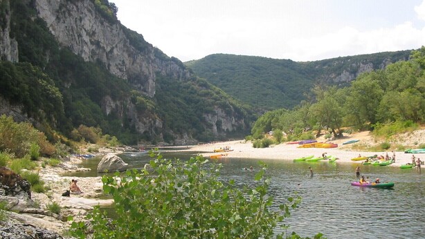 Un fiume con kayak e persone, circondato da scogliere e vegetazione.