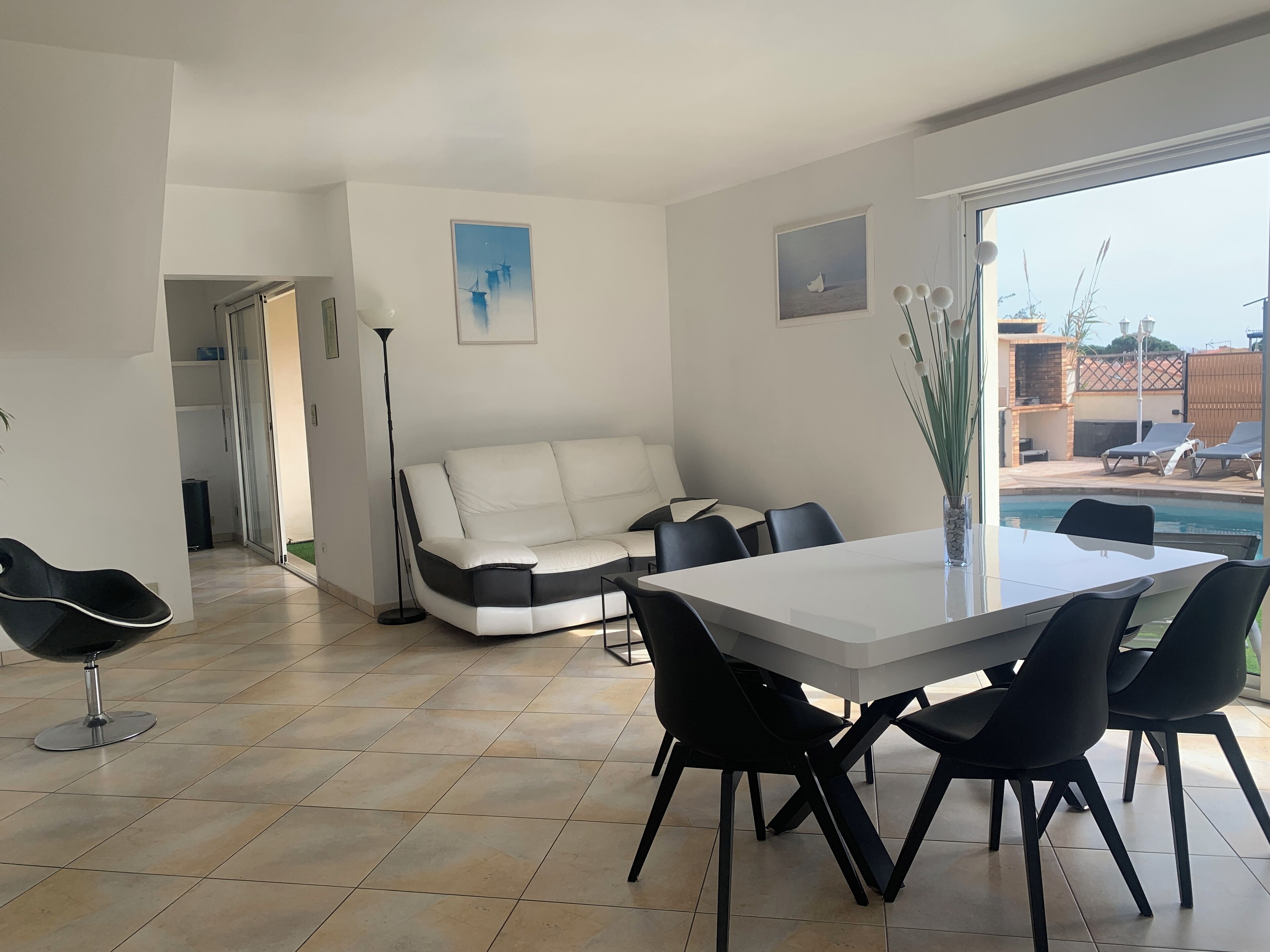 Een moderne woonkamer met een witte bank, zwarte stoelen, een glazen eettafel en uitzicht op een zwembad.