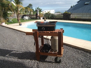 A portable grill with a gas tank and a table, placed on a gravel surface near a swimming pool. - apartment rental Le Tampon (Réunion) (LE TAMPON)