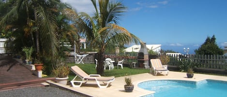 A pool area with lounge chairs, a barbecue grill, and palm trees.
