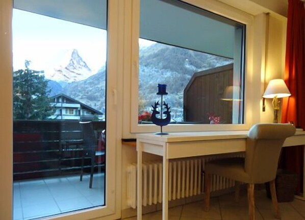 A room with a large window overlooking a mountain, a radiator, a desk with a chair, and a lamp. - Zermatt centre - High standing all mod cons rental - View of the Cervin (Zermatt)