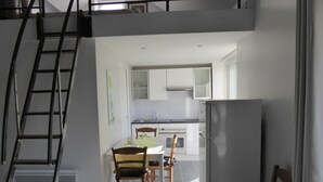 A modern kitchen with white cabinets, a stainless steel sink, and a built-in oven. There is a dining area with a table and chairs, and a staircase leading to an upper level. - Charming country house (Andonville)