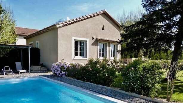 Une maison avec une piscine, un patio couvert et un jardin fleuri.