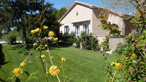 Une maison avec une pelouse bien entretenue, un grand arbre et des plantes en fleurs au premier plan.