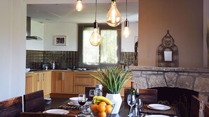 A dining area with a table set for two, a kitchen in the background, and a stone fireplace. - Villa Angel - Panoramic view with magnificent swimming pool and pool house (La Gaude)