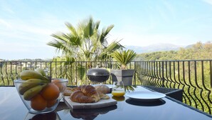 A table with a fruit bowl, croissants, and juice, overlooking a scenic view with palm trees and mountains. - Villa Angel - Panoramic view with magnificent swimming pool and pool house (La Gaude)