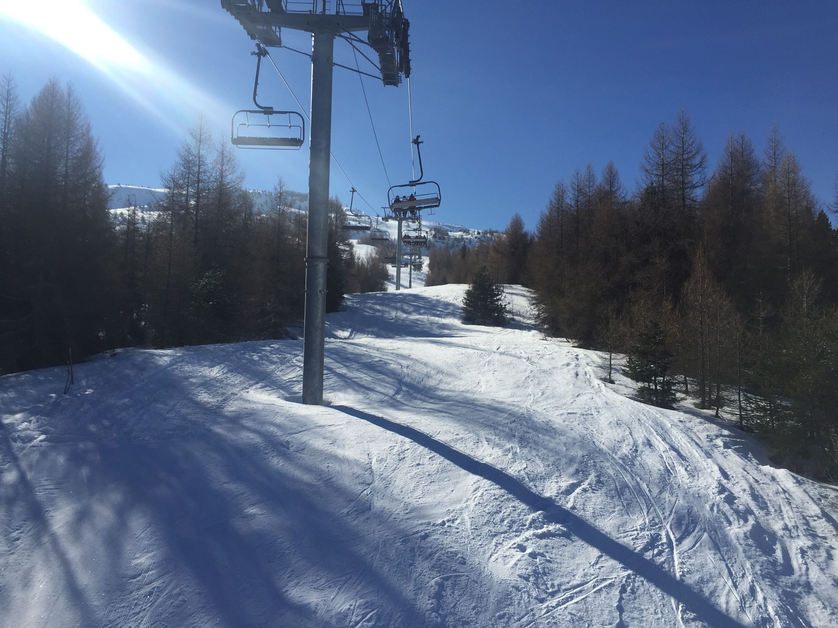 En skilift med stole, der bevæger sig op og ned ad en sneklædt skråning, omgivet af træer.