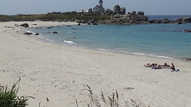 Una playa con un faro y afloramientos rocosos.