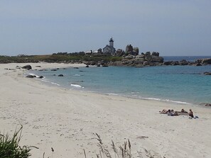 A beach with a lighthouse and rocky outcrops.