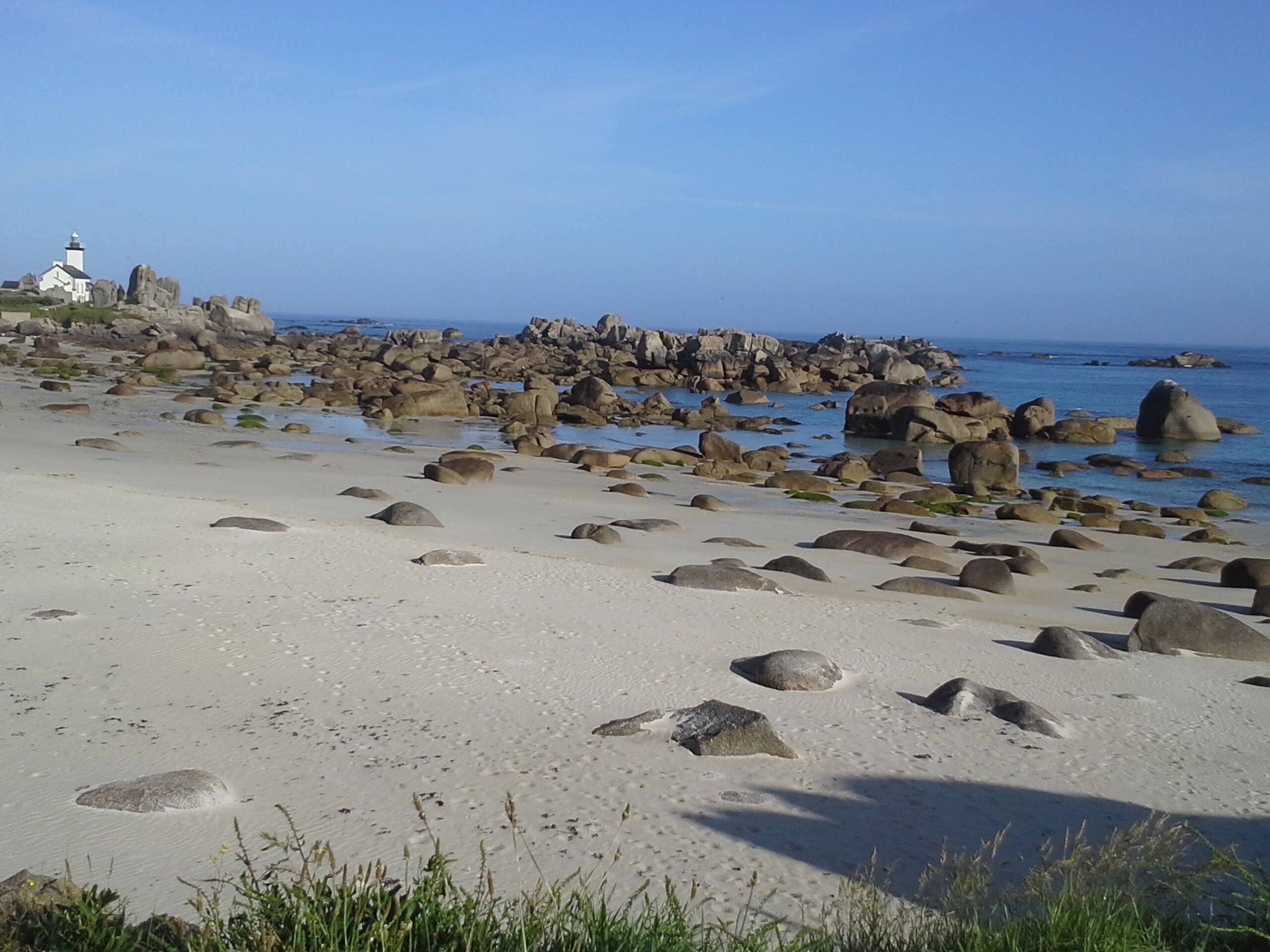 A beach with large rocks and a lighthouse in the background.