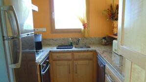 Una cocina compacta con armarios de madera, un refrigerador de acero inoxidable, un lavamanos y una ventana con cortinas.