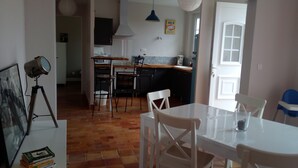 A dining area with a white table and chairs, a kitchen in the background, and a door leading outside.