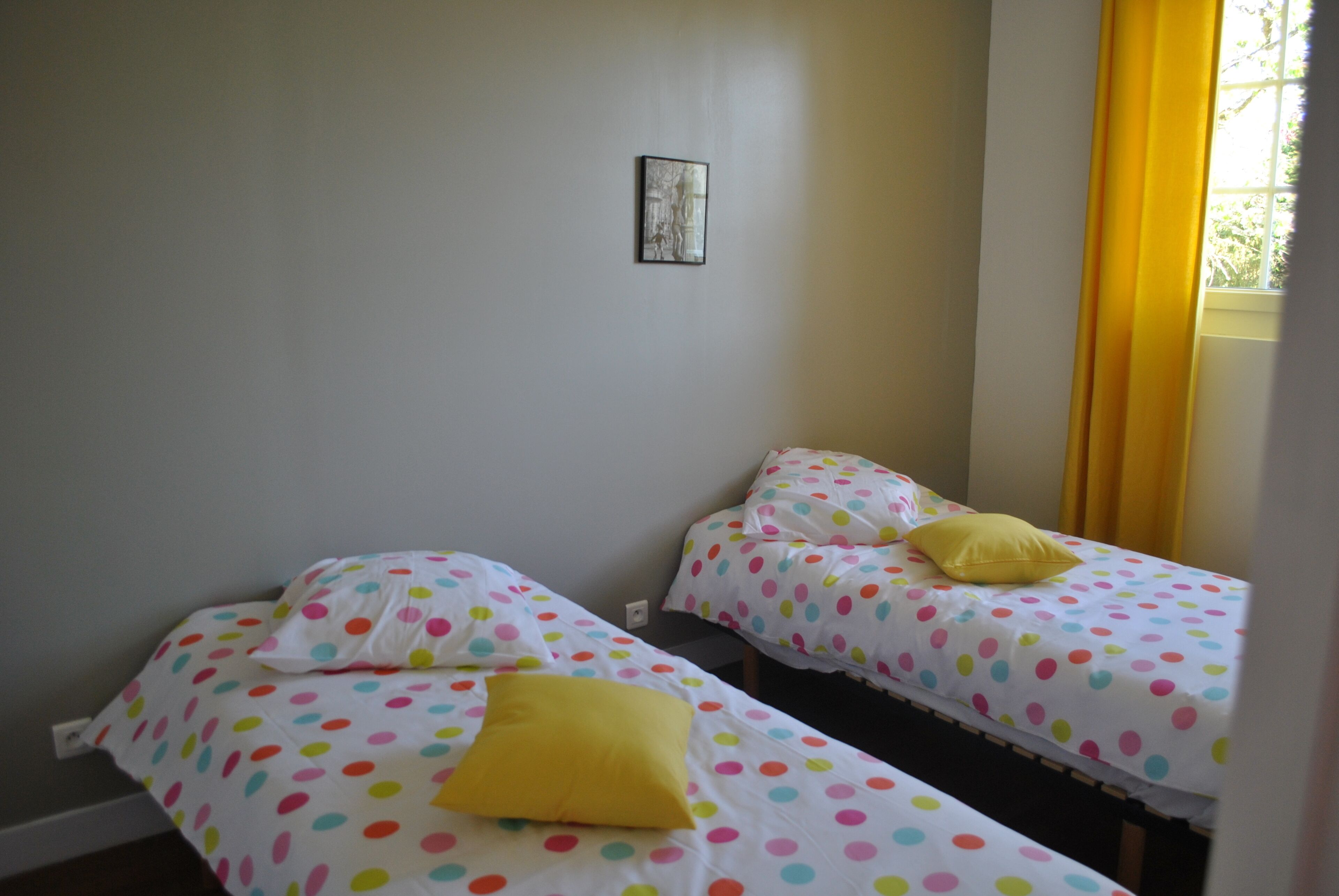 A room with two beds, each with colorful polka dot bedding and a yellow pillow.
