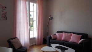 A living room with a sofa, two white tables, a chair, and a pink ottoman.