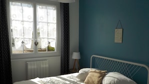 A bedroom with a bed, a window with curtains, a radiator, a bedside lamp, and a wall-mounted sign.