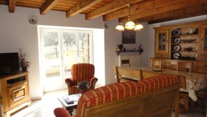 Un salon chaleureux avec un plafond en bois, un canapé, un téléviseur et un coin repas comprenant une table et des chaises.
