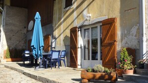 Un espace extérieur aménagé dans un style rustique, avec une table et des chaises, un parasol bleu et des plantes en pot.