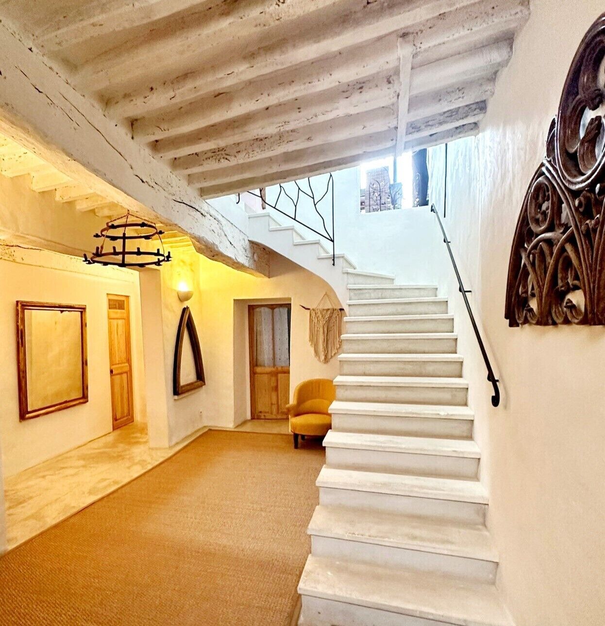 A spacious interior with a white staircase leading to a second floor, a wooden door, and a yellow armchair.