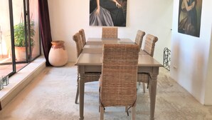 Un coin repas avec une table et des chaises en osier, une plante en pot et deux tableaux accrochés au mur.