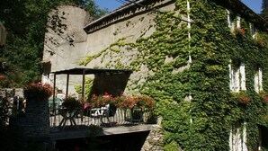 A building with ivy-covered walls and a covered outdoor seating area with tables and chairs. - Family Castle Life  (Mérial)