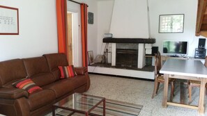 A living room with a brown sofa, a glass coffee table, a fireplace, a TV, and a dining table with chairs. - HOUSE IN THE HEART OF THE VALLEYS CEVENOLES large pool access (Chambon)