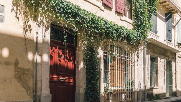 A building with a red door, a metal gate, and a balcony with potted plants. - Charming studio 2 minutes from the Arena (Arles)