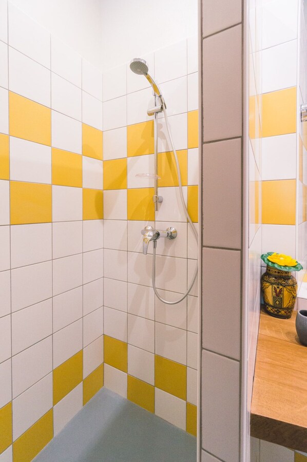 Une douche avec un mur recouvert de carreaux jaunes et blancs formant un motif à carreaux, un pommeau de douche et un flexible de douche.