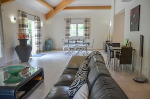 A modern living room with a leather sofa, a glass coffee table, and a dining area with a table and chairs.