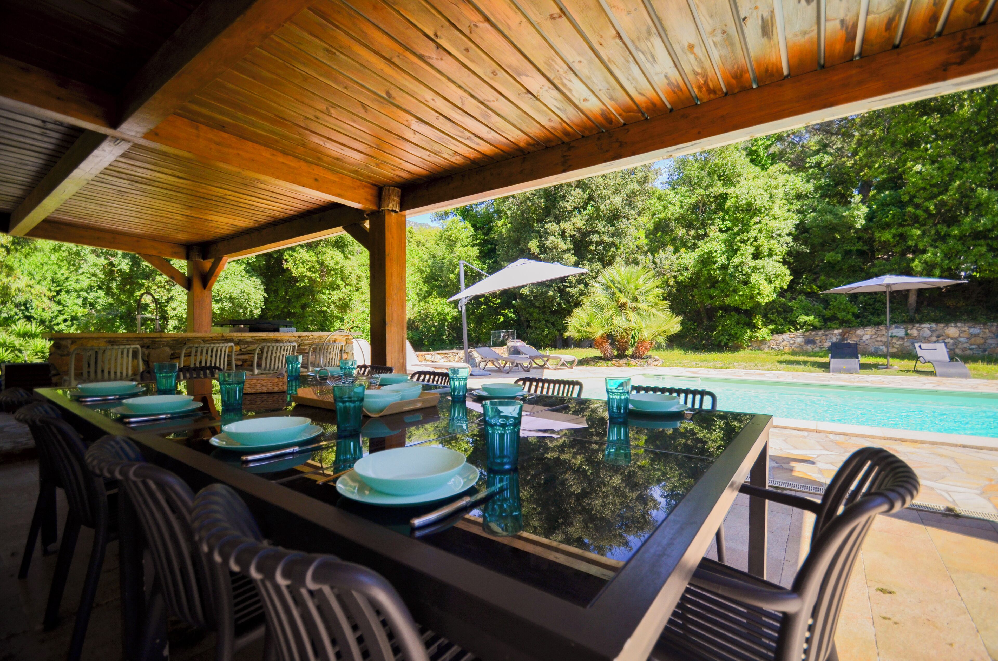 Ein Essbereich im Freien mit Blick auf einen Pool, einer Holzpergola und Liegestühlen.