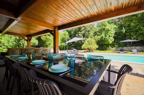 An outdoor dining area with a pool view, wooden pergola, and lounge chairs.