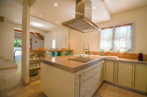 A modern kitchen with a central island, built-in cabinets, and a window with curtains. - Modern Villa With Heated Pool - Saint Florent - (Saint-Florent)
