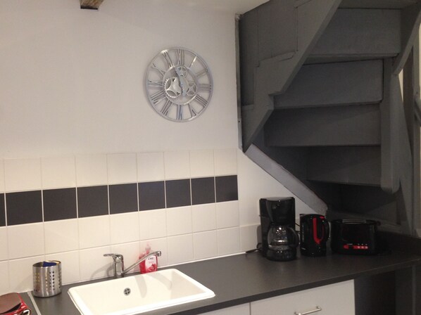 A kitchen with a white sink, a clock, a coffee maker, and a toaster on the counter. - Located in the inner city of Honfleur, with aspect of both town house and apt. (Honfleur)